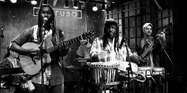Dans un bar, un groupe de musique exotique joue d'un instrument de percussion et une guitare devant les yeux d'un public.