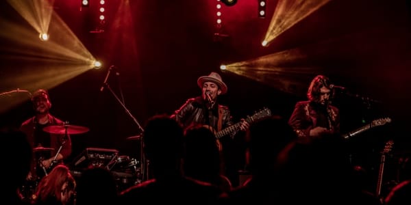 Un guitariste qui porte un chapeau et joue de son instrument sur scène lors d'une animation en soirée.